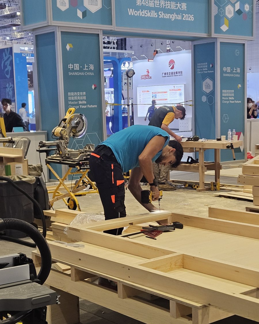 A competitor screws together a timber frame beneath the WorldSkills arch in Shanghai 2026